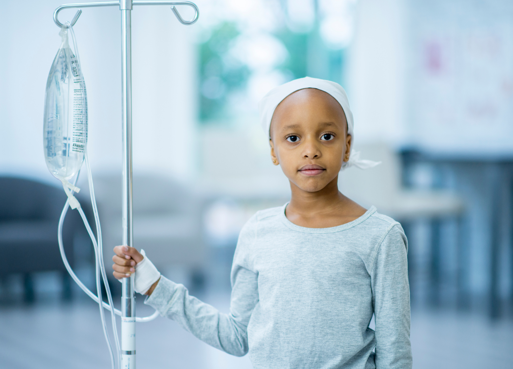 Young girl with a headscarf holding an IV pole in a hospital setting
