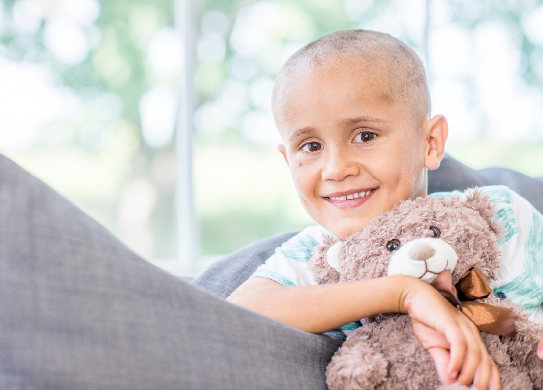 Child patient holding a teddy bear, sitting on a couch outdoors.