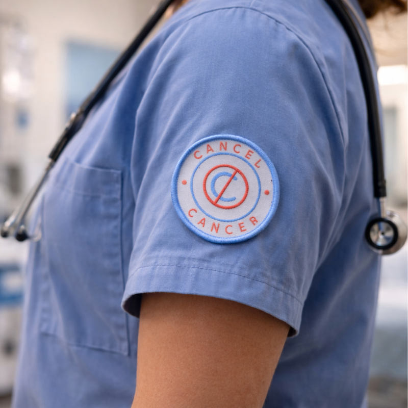 Person wearing a blue scrub top with a 'Cancel Cancer' patch on an arm.
