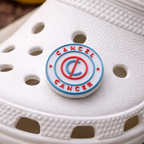 White sandal with a 'Cancel Cancer' charm on a wooden surface