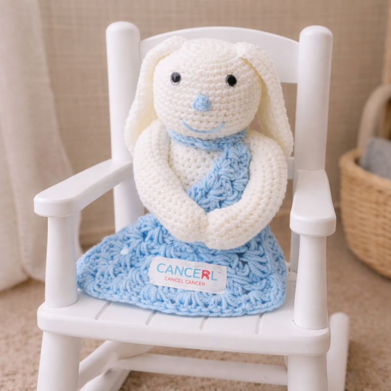 Crocheted bunny toy with a blue scarf on a white chair, featuring the Cancer Cancer logo.