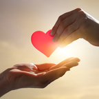 Two hands reaching towards a glowing red heart against a warm background