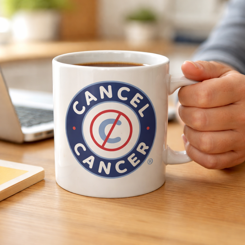 Person holding a mug with 'Cancel Cancer' logo on a desk.